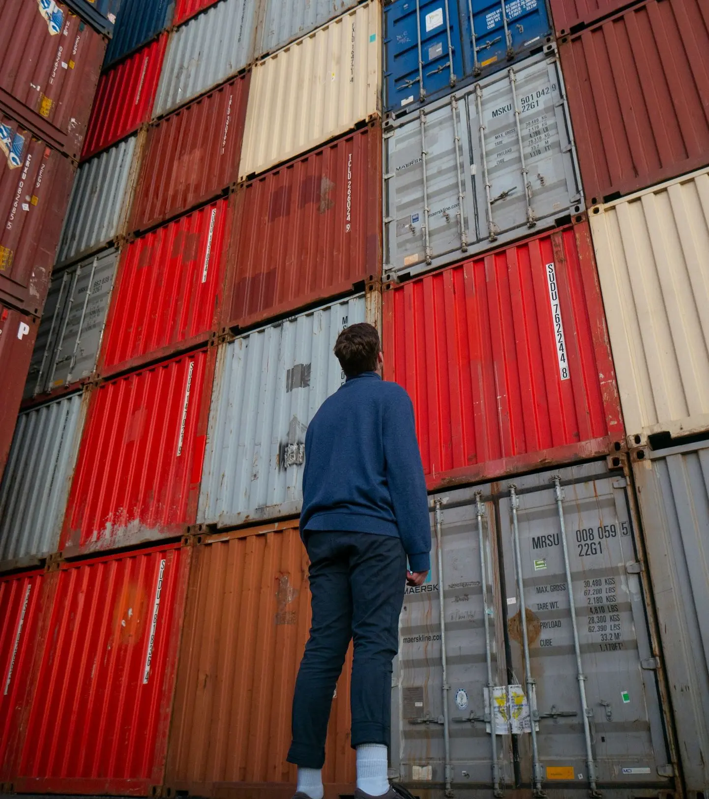 man in blue long sleeve shirt standing in front of red and blue intermodal containers